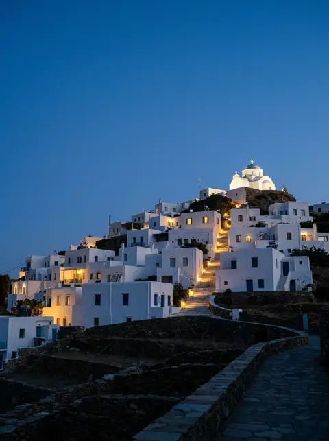 Hilltop village of Ios at dusk with warm lights climbing toward the chapel