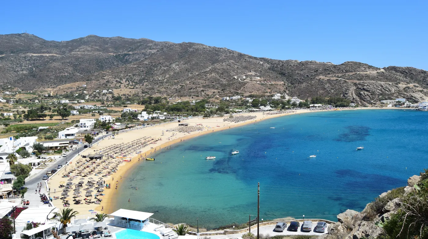 The full sweep of Mylopotas beach on Ios, sunbeds thinning towards the headland