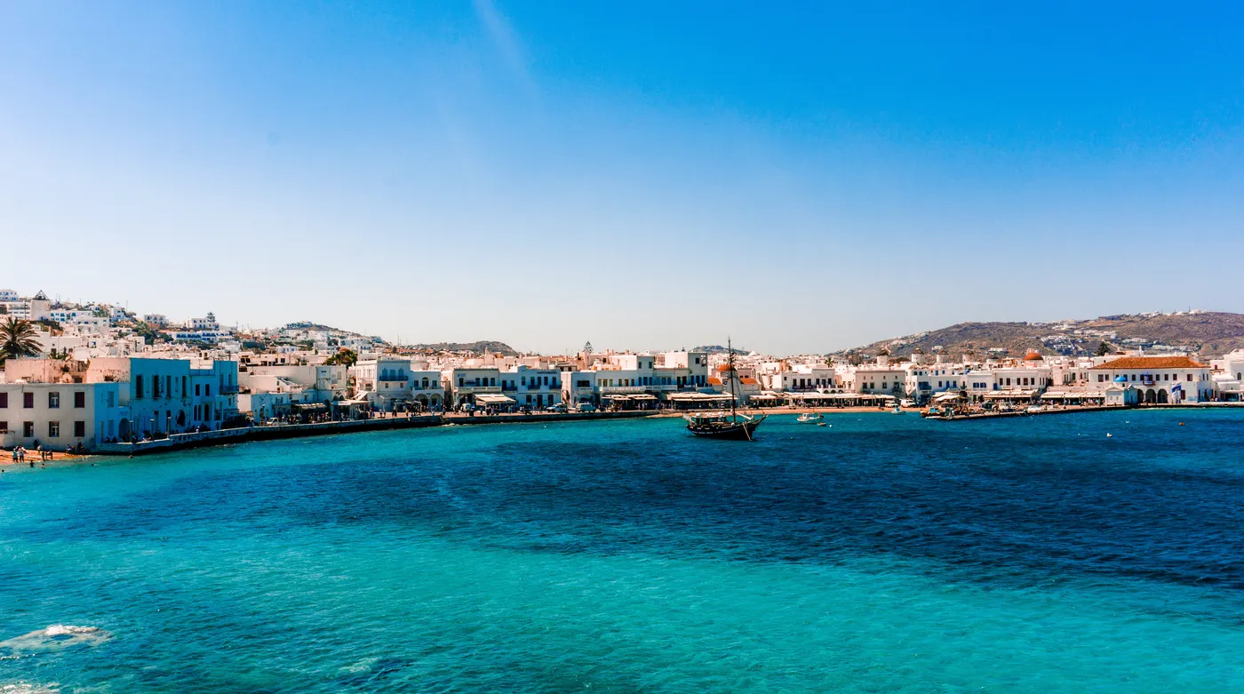 A Cycladic town along its old port, whitewashed houses against a teal sea