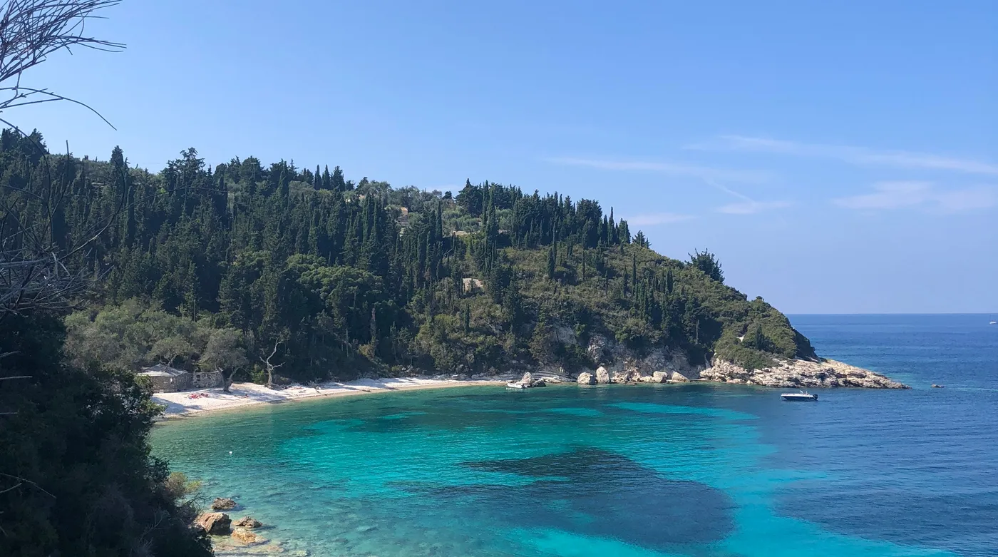 A pine-backed cove on Paxos, electric blue water over white stones