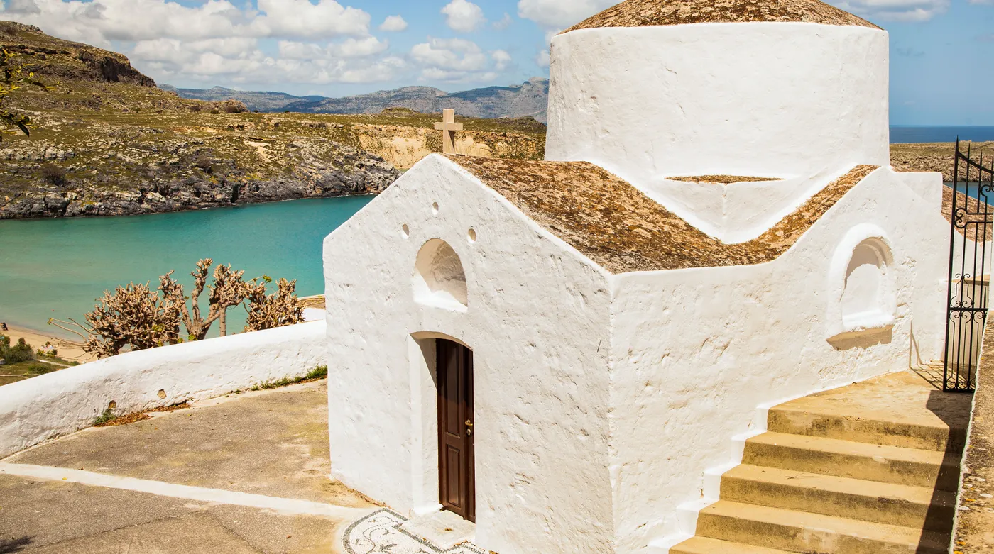 A white chapel above a turquoise bay in the Dodecanese