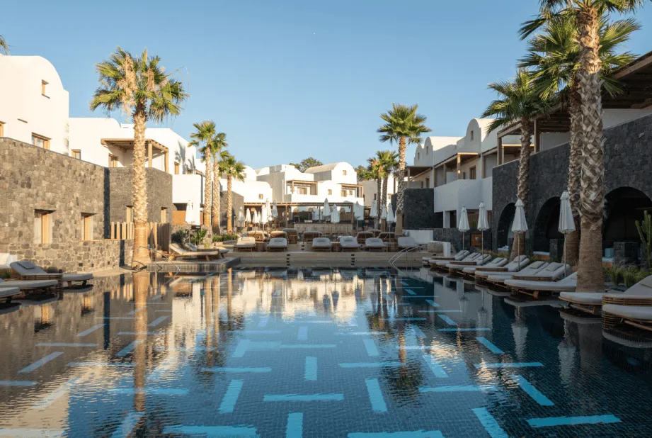 The pool courtyard at Radisson Blu Zaffron Resort in Kamari, black volcanic stone arcades and palm trees around a geometric-tiled pool